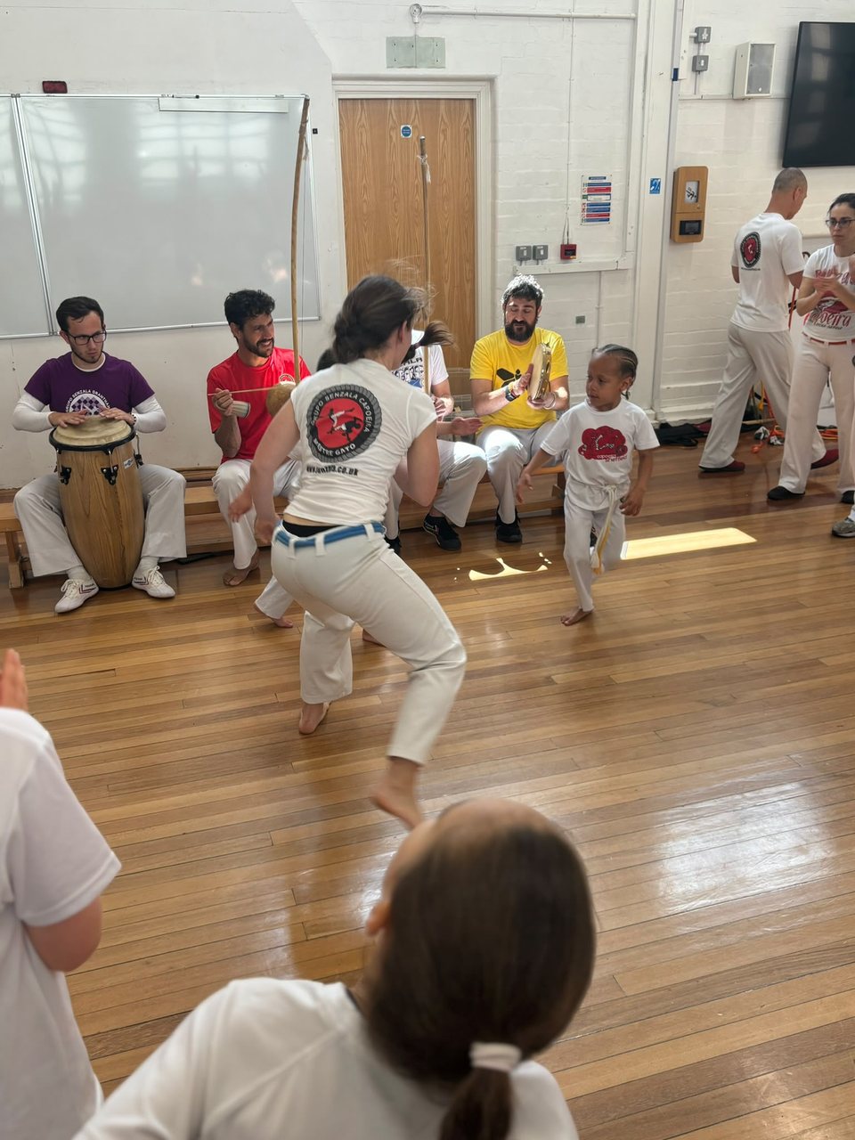 A capoeirista wearing a red Senzala emblem plays in front of the musicians.